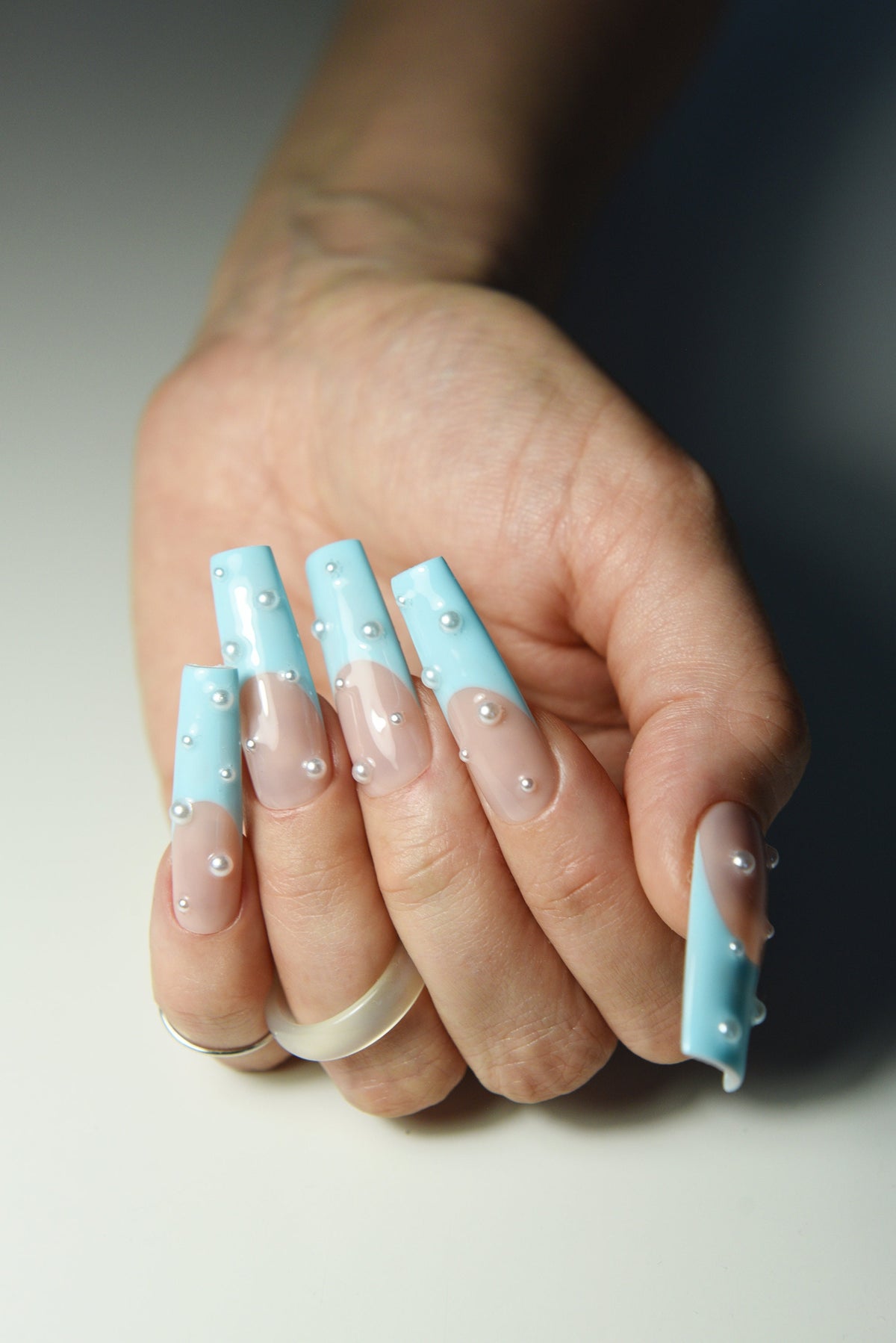 Pastel blue French press-on nails with pearl accents, side angle