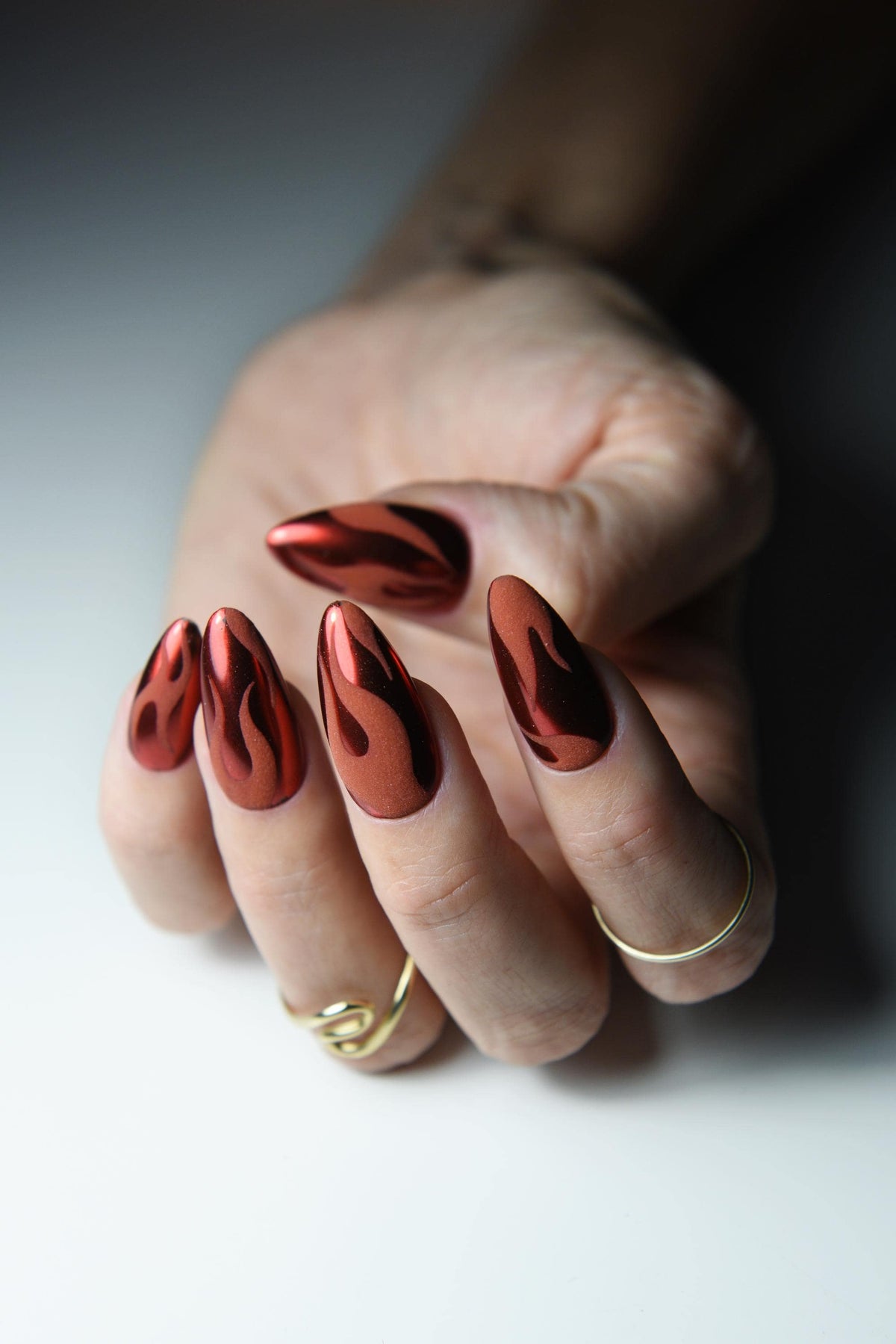 Warm red chrome press-on nails with matte black flame design – detail view