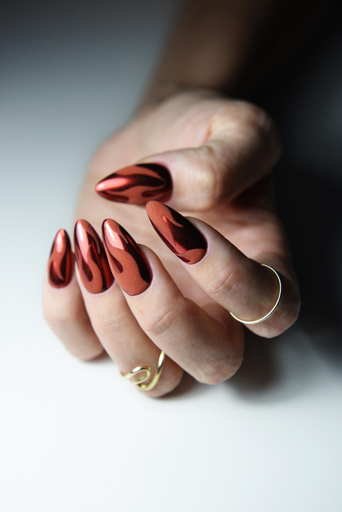 Warm red chrome press-on nails with matte black flame design – detail view