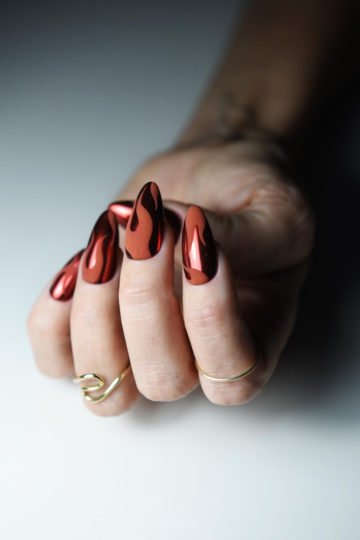 Warm red chrome press-on nails with matte black flame design – detail view