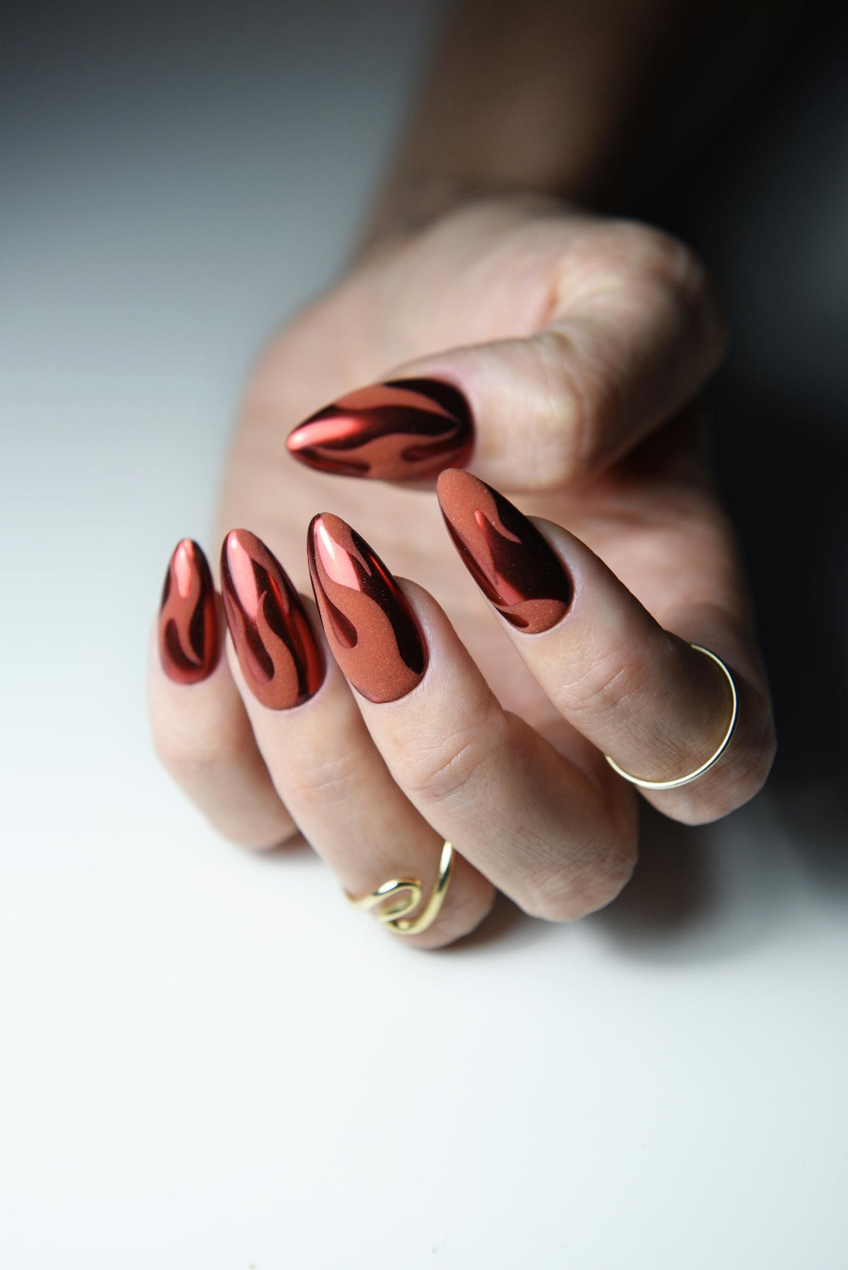 Warm red chrome press-on nails with matte black flame design – detail view