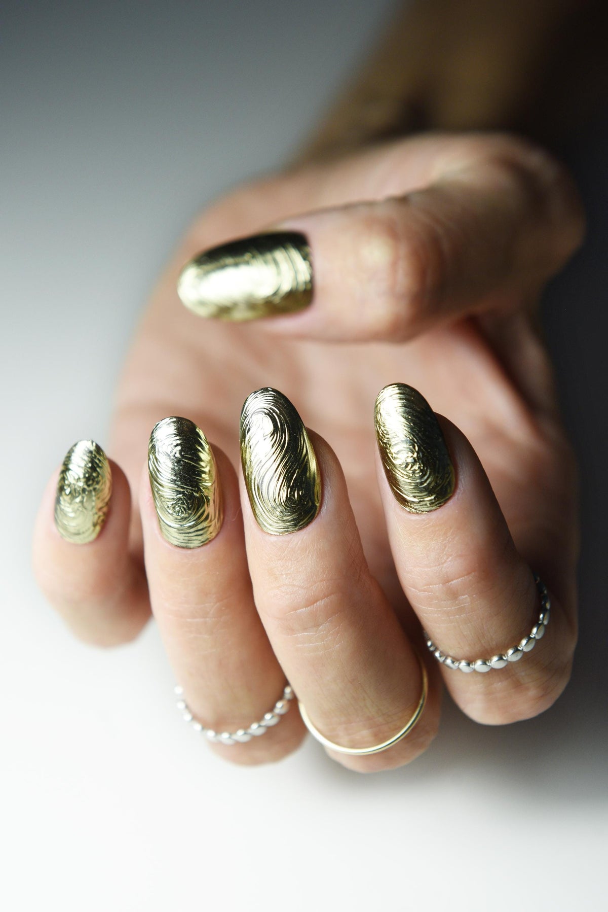 Sculpted gold chrome swirl press-on nails with liquid-metal texture – detail view