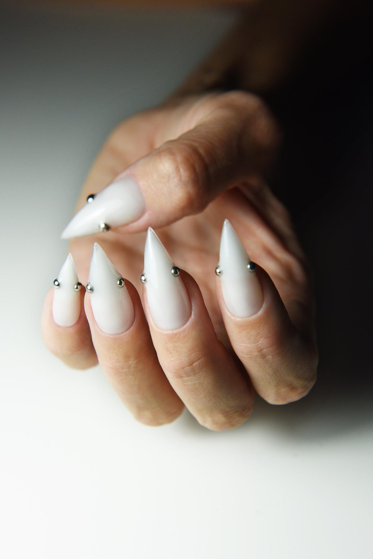 Milky white press-on nails with small metallic piercing studs – detail view