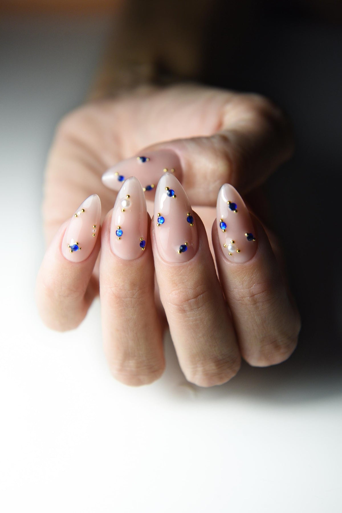Milky nude press-on nails with sapphire blue crystals and gold accents