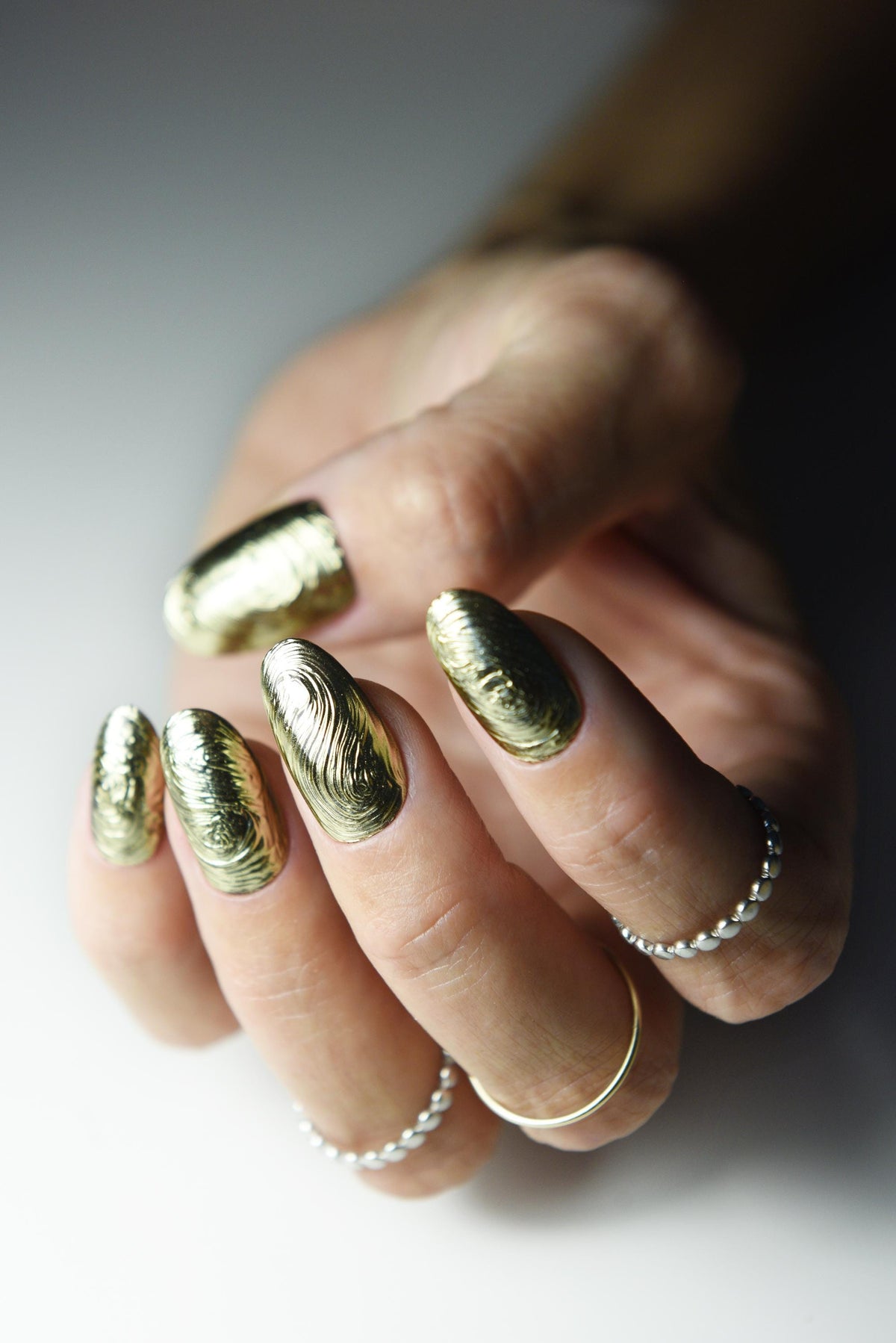 Sculpted gold chrome swirl press-on nails with liquid-metal texture – detail view