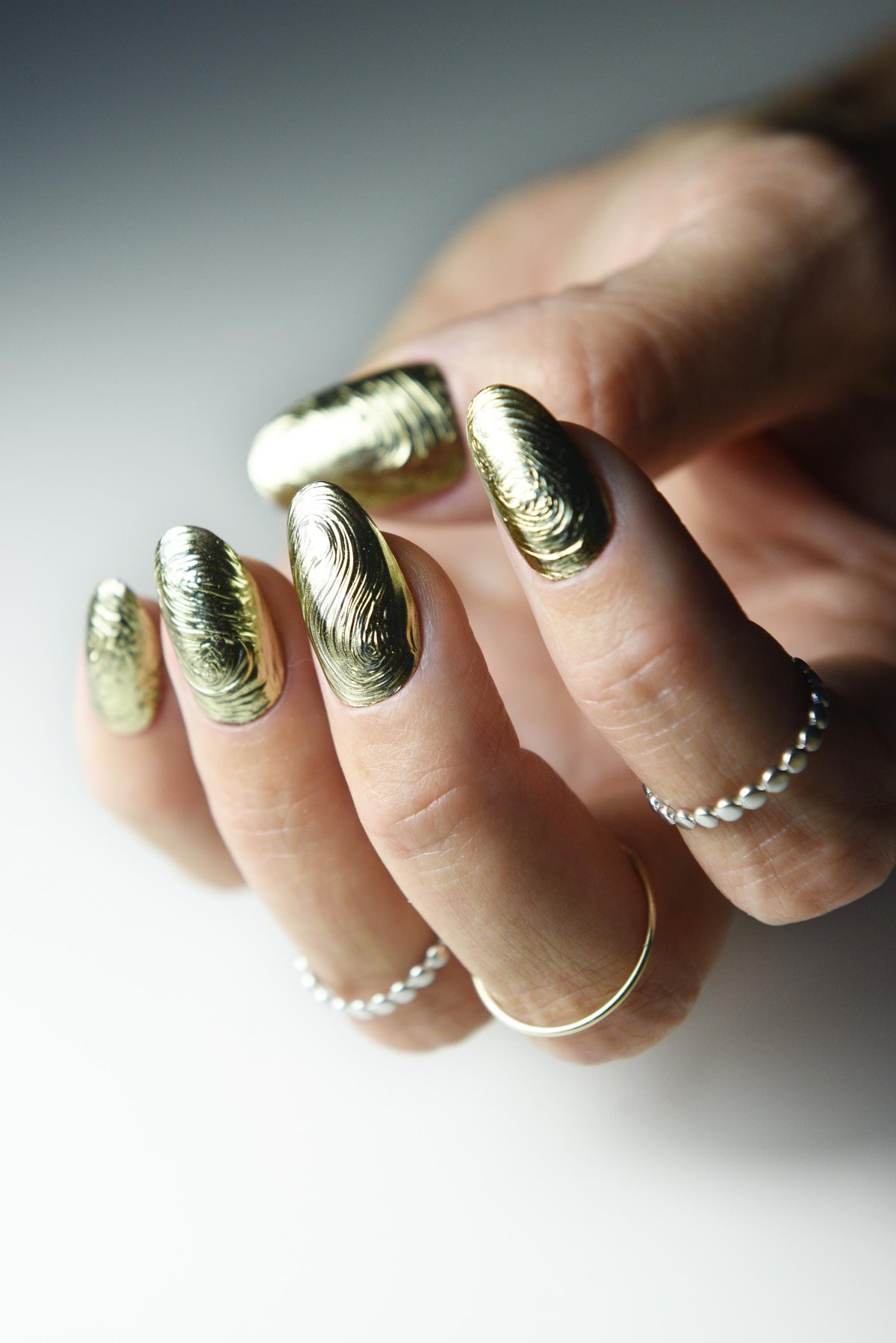 Sculpted gold chrome swirl press-on nails with liquid-metal texture