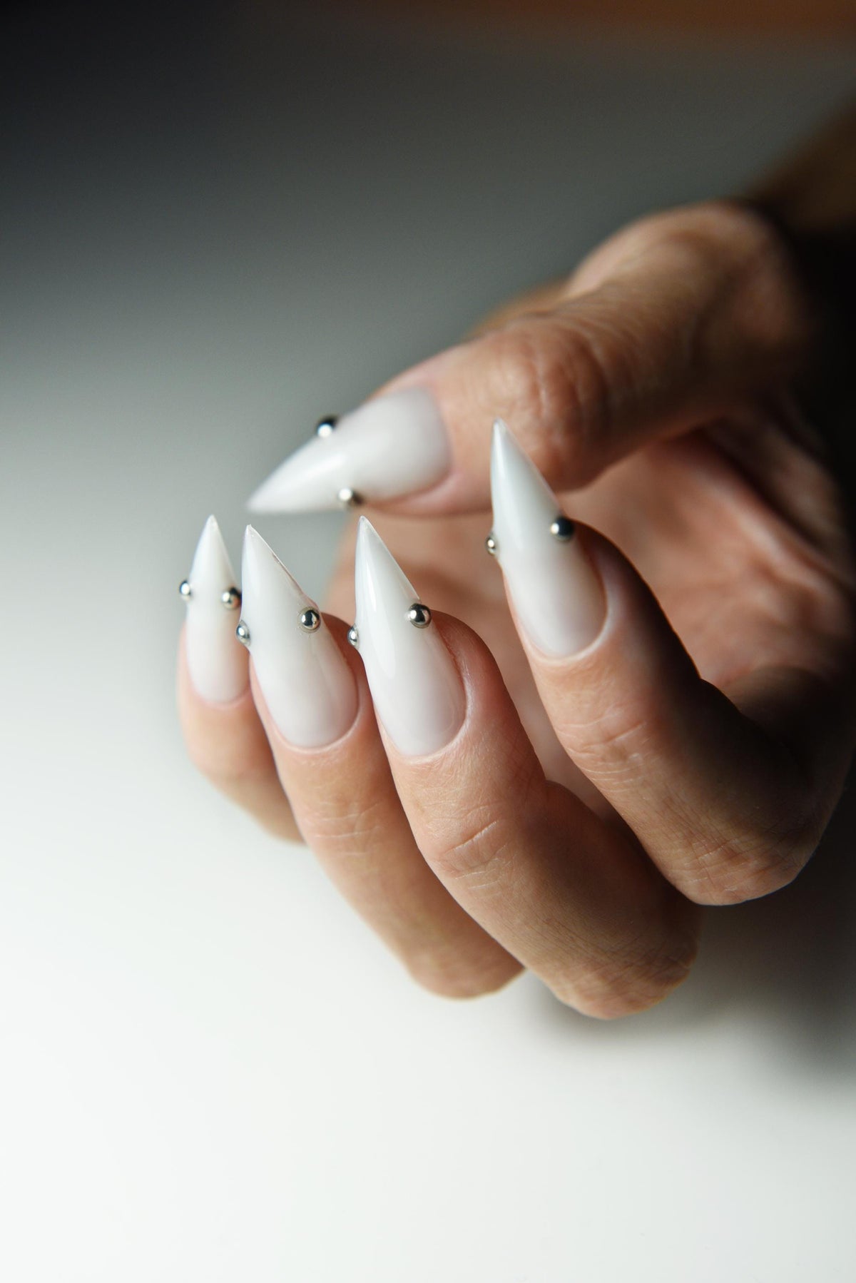 Milky white press-on nails with small metallic piercing studs – detail view