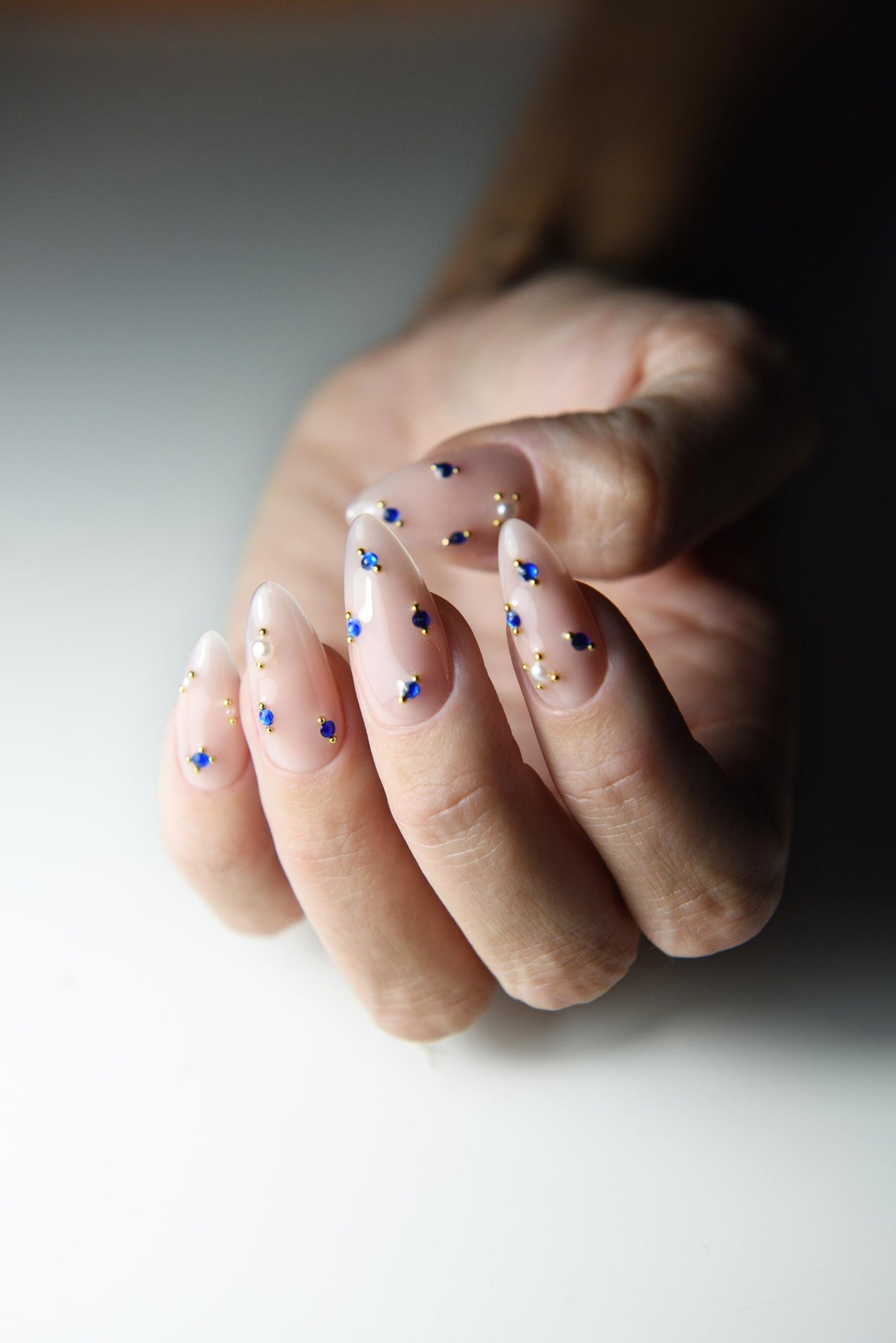 Milky nude press-on nails with sapphire blue crystals and gold accents – detail view